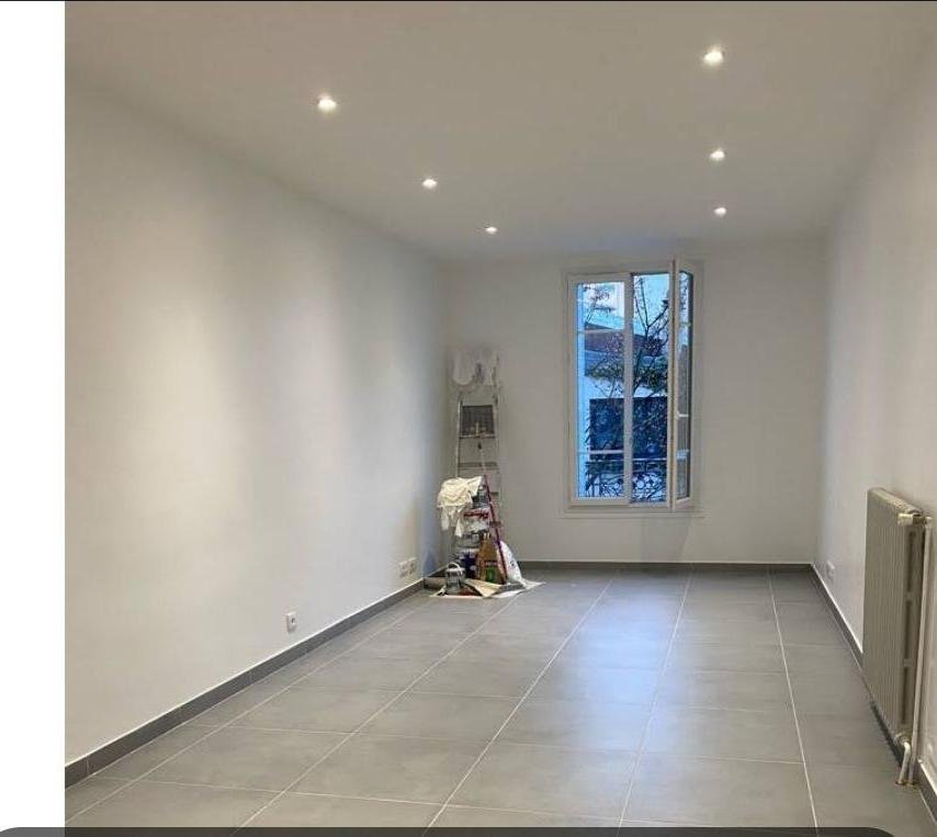 Séjour après rénovation : murs blancs, spots encastrés, grand carrelage gris